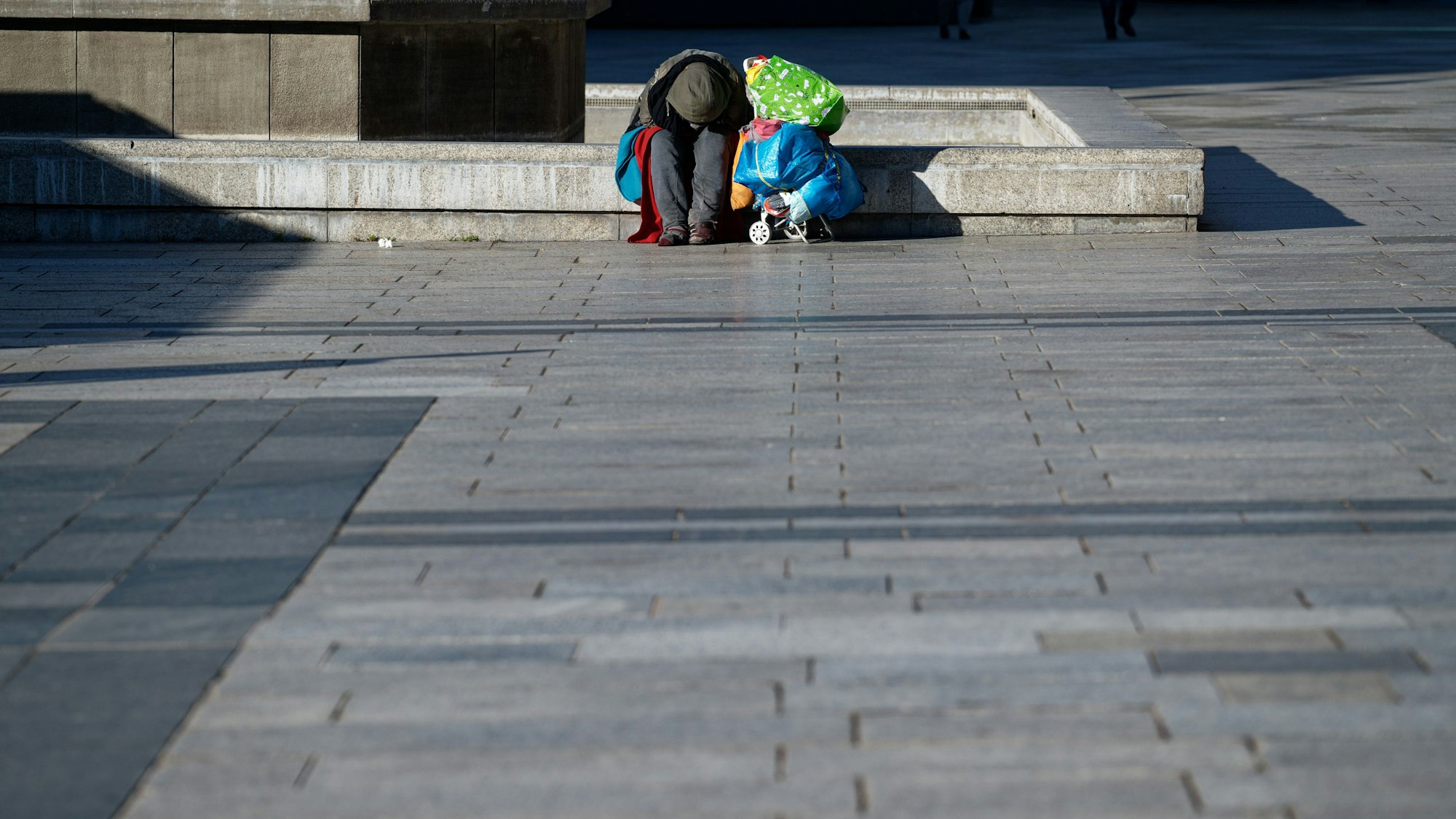 Ein Obdachloser wärmt sich auf dem Roncalliplatz vor dem Kölner Dom sitzend in der Sonne. (Symbolfoto)