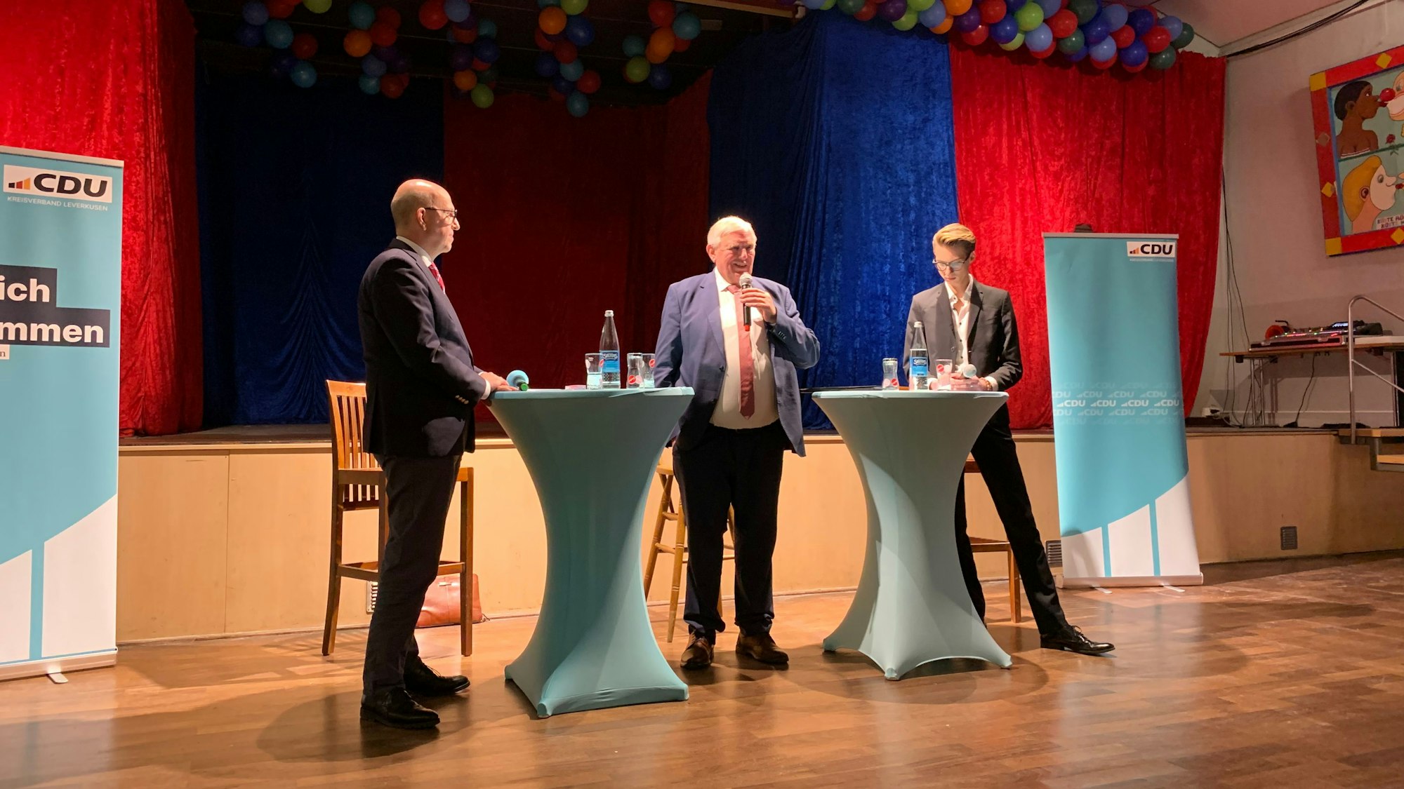Drei Männer stehen nebeneinander an Tischen.