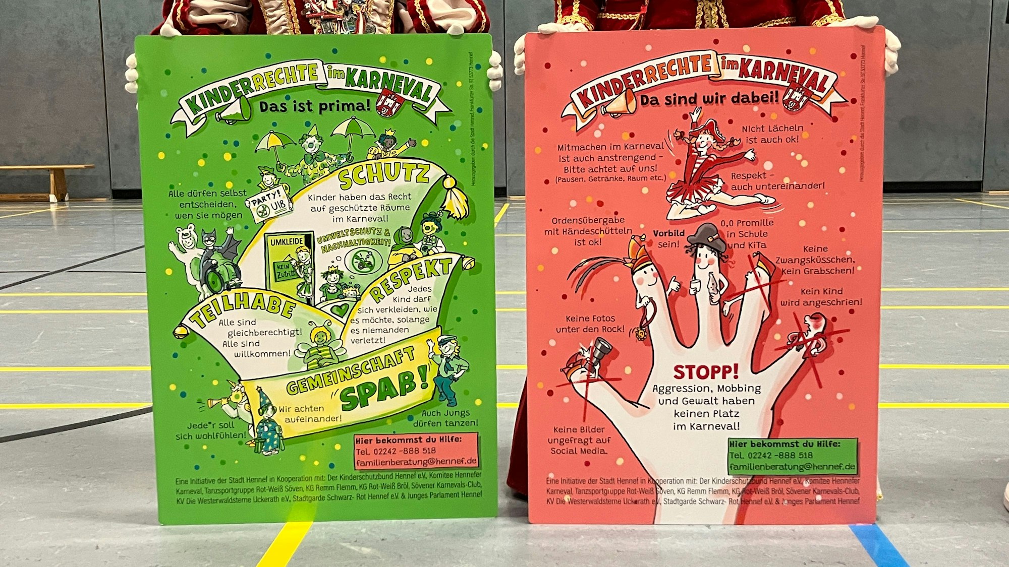 Auf zwei Plakaten, rot und grün, wird auf die Kinderrechte im Karneval aufmerksam gemacht.