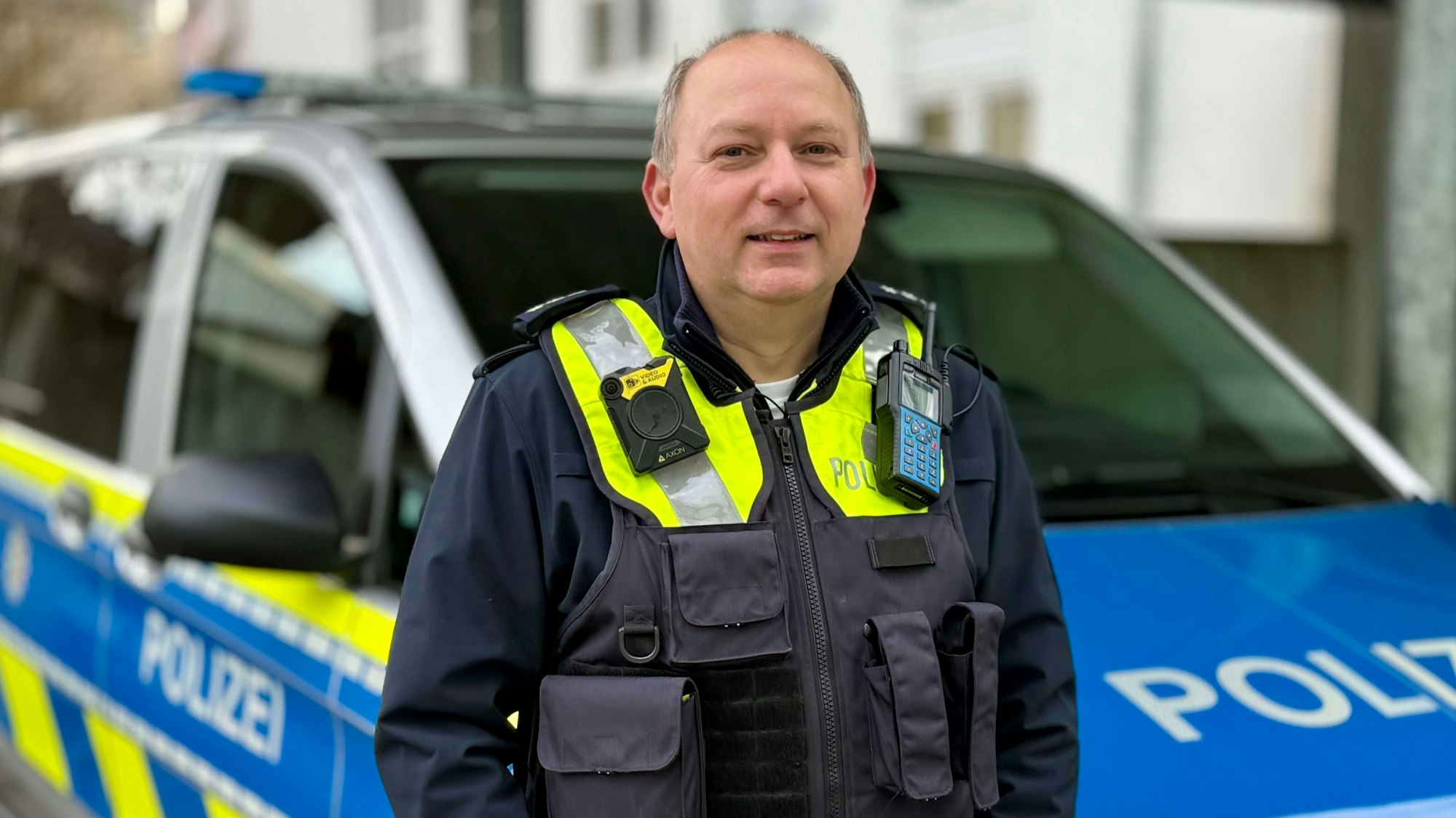 Ein Polizist steht vor einem Streifenwagen.