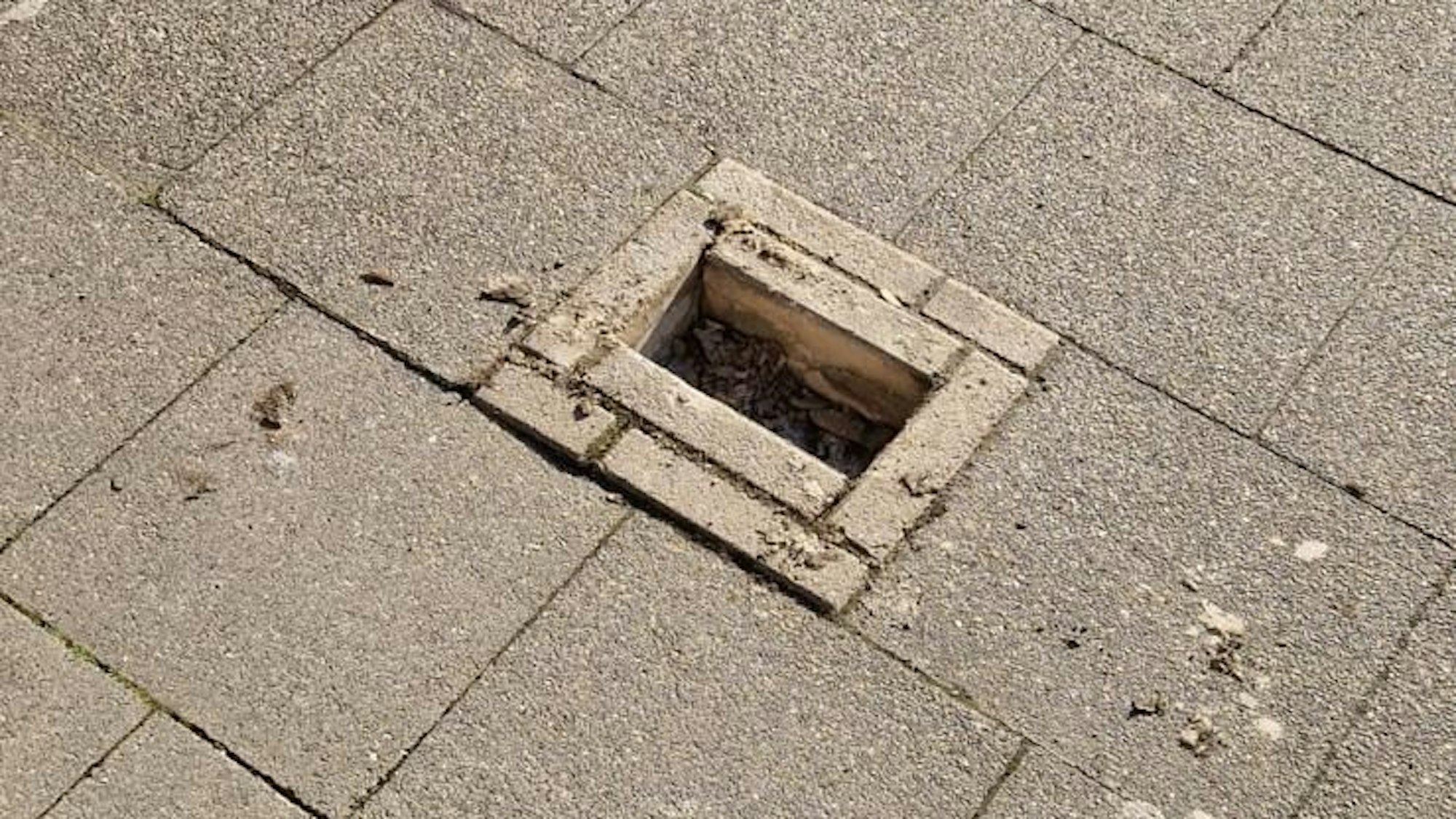 Zu sehen ist eine Lücke in einem Gehwegpflaster, in dem Steine fehlen.