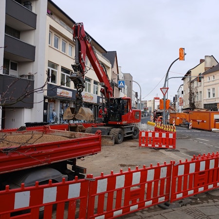 Eine Straßenbaustelle mit Absperrungen und Bagger.