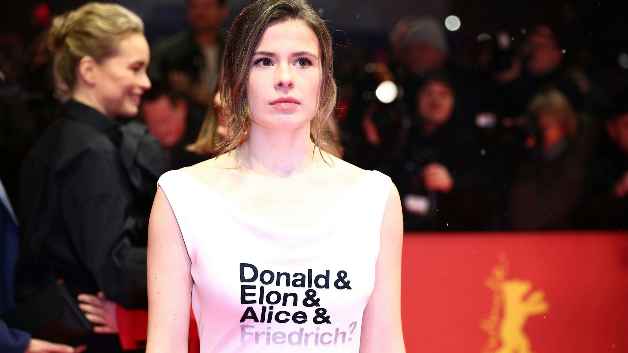 Luisa Neubauer, Aktivistin, steht am Eröffnungsabend der Berlinale auf dem Roten Teppich und trägt ein Kleid mit der Aufschrift „Donald & Elon & Alice & Friedrich?“.