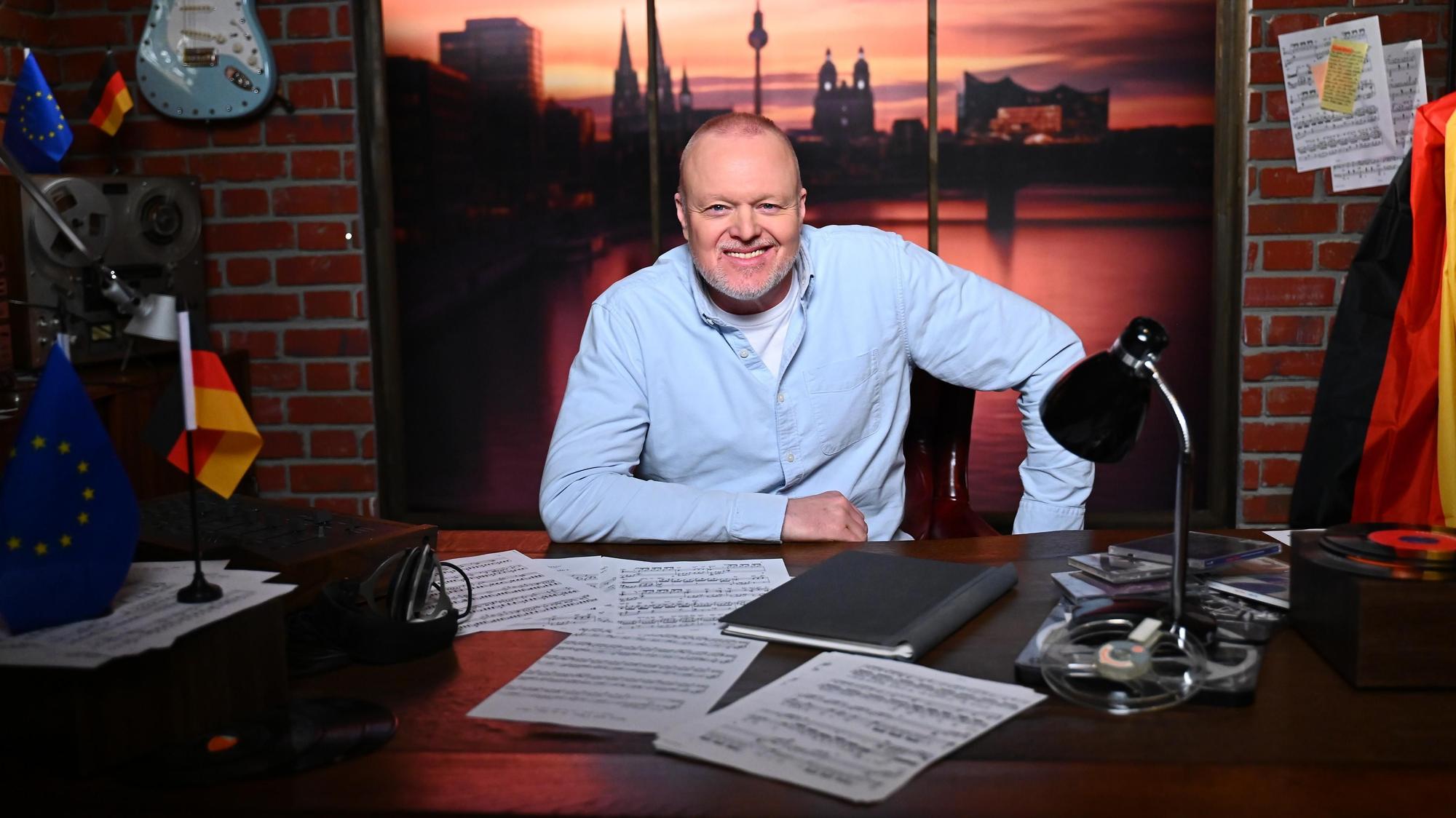 Stefan Raab sitzt an einem Schreibtisch.