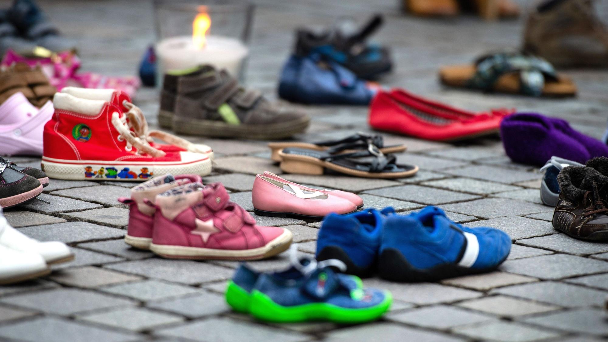 Verschiedene Schuhe von Kindern und Jugendlichen stehen auf dem Boden, dahinter ist eine Kerze zu sehen.