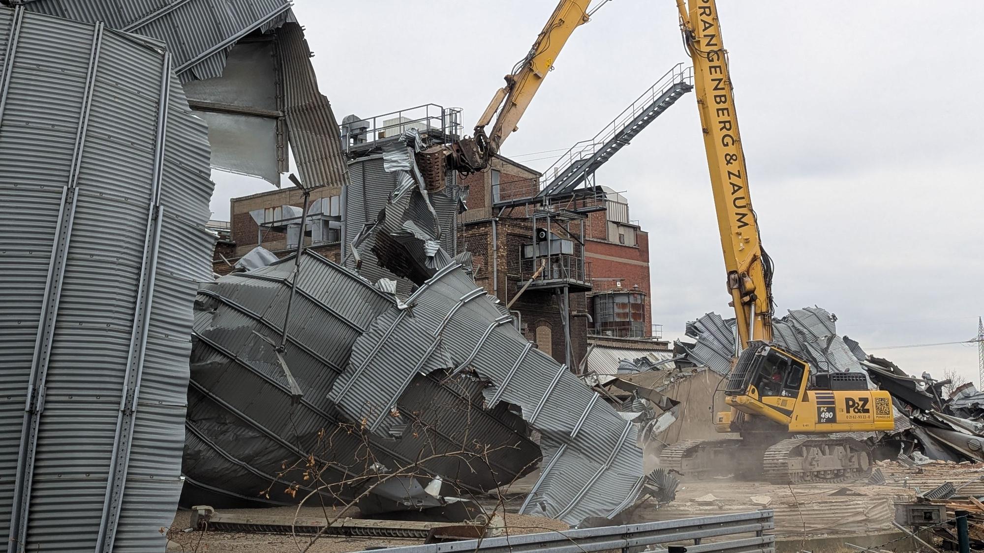 Das Foto zeigt einen Bagger, dessen Greifer ein altes Blechsilo auseinanderreißt.