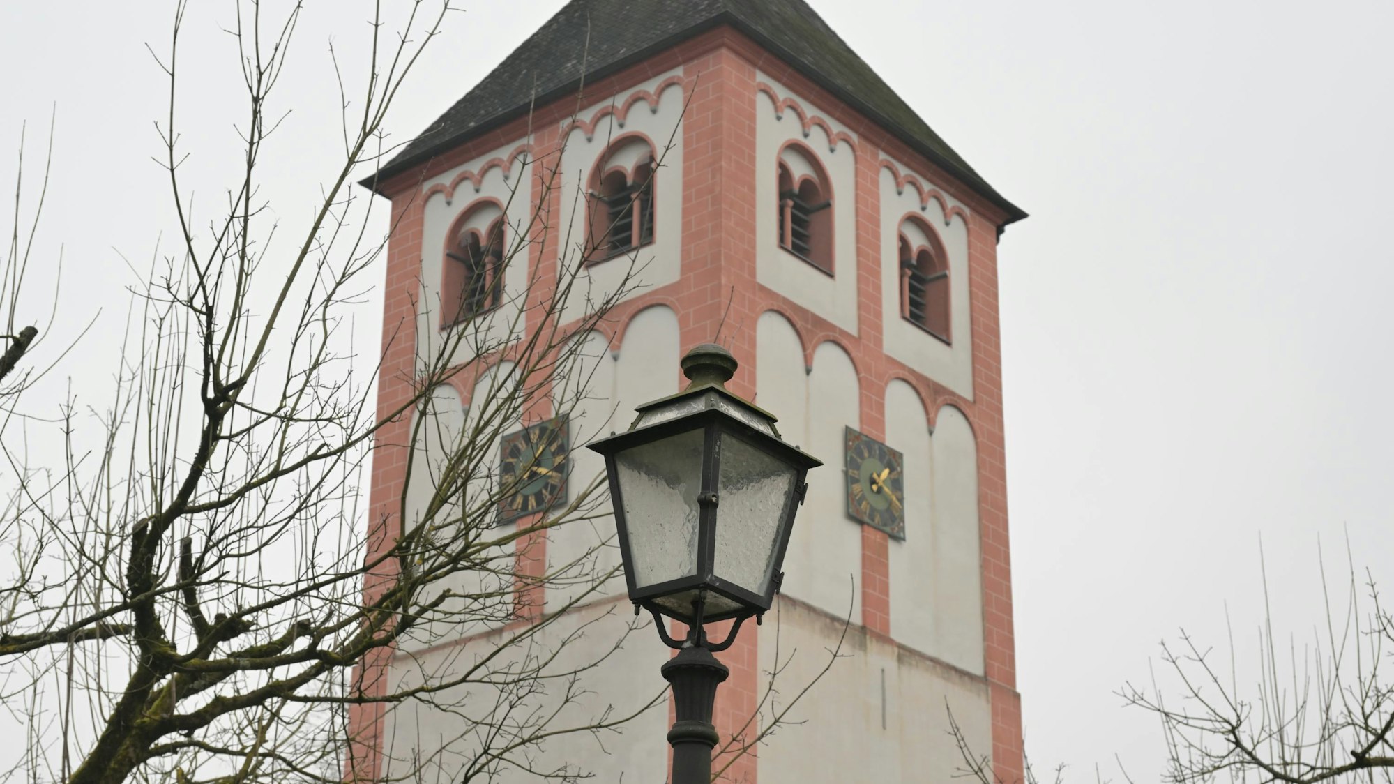 Eine historische Straßenlaterne steht vor einem Kirchturm.