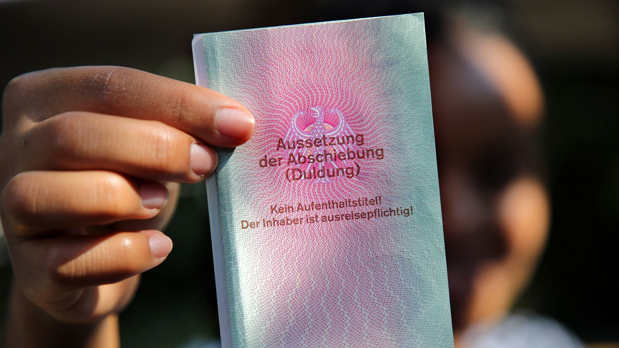 Eine junge Frau aus Afrika hält einen Ausweis für Flüchtlinge in der Hand mit dem Titel: Aussetzung der Abschiebung (Duldung).