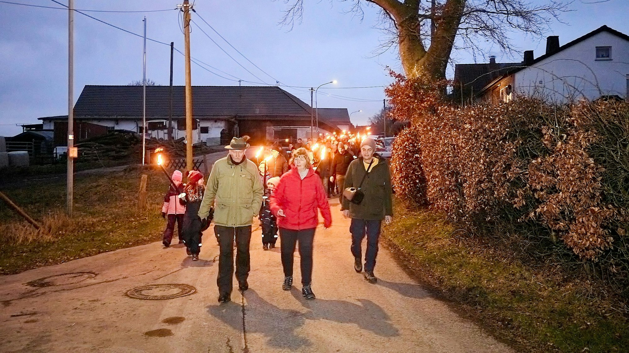 Eine Gruppe Leute läuft mit Fackeln in der Hand über eine Dorfstraße.