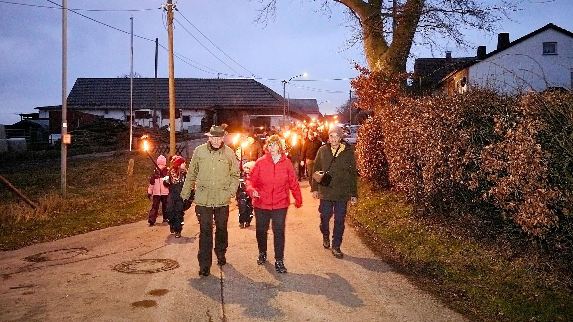 Eine Gruppe Leute läuft mit Fackeln in der Hand über eine Dorfstraße.