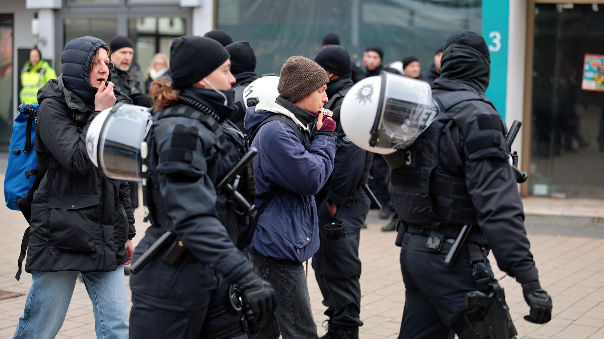 Polizisten geleiten zwei Personen mit Trillerpfeifen vom Ort der AfD-Wahlkampfveranstaltung in Euskirchen weg.