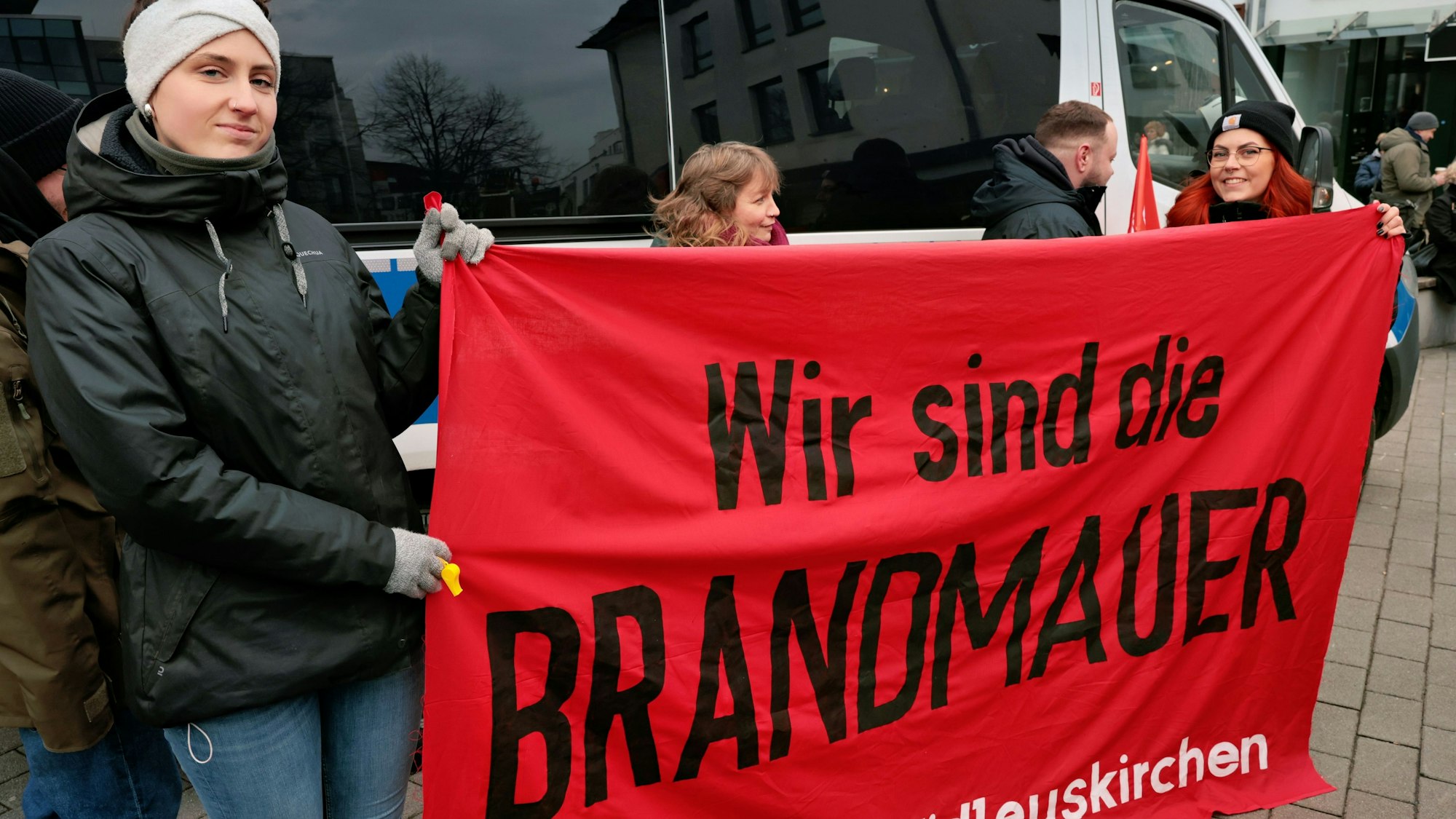 Teilnehmer der Demonstration in Euskirchen für Freiheit und Demokratie halten ein rotes Transparent, auf dem in schwarzen Buchstaben steht „Wir sind die Brandmauer“.