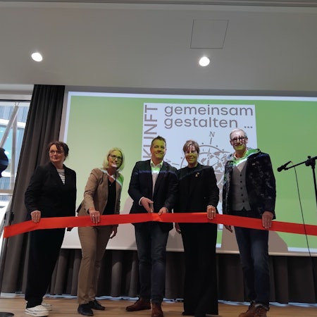 Fünf Personen durchschneiden auf einer Bühne ein rotes Band