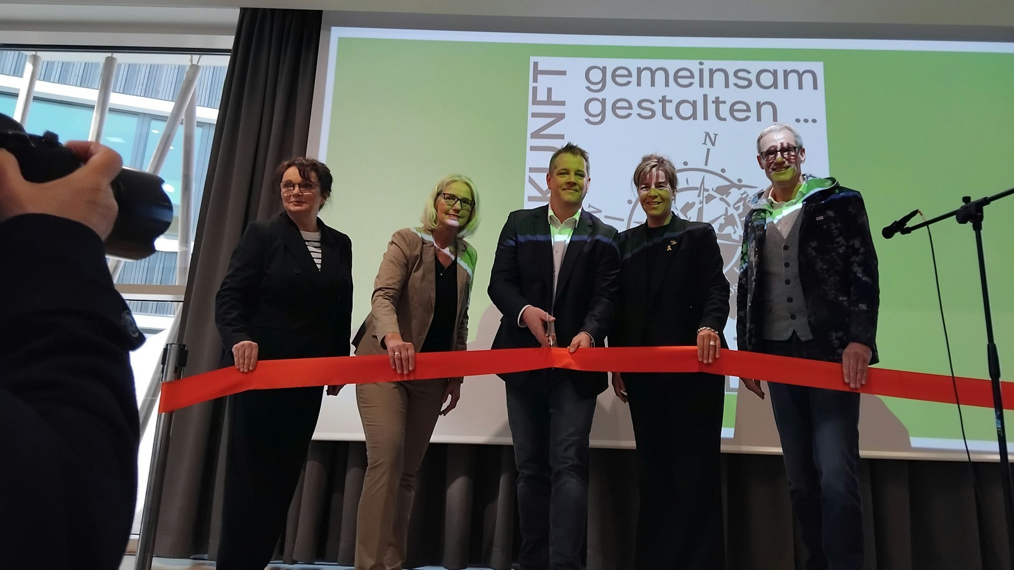 Fünf Personen durchschneiden auf einer Bühne ein rotes Band