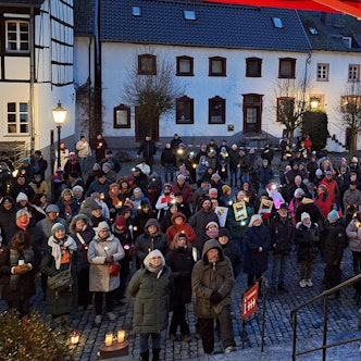 Ein Redner steht an einem Stehpult auf einer Bühne. Vor ihm auf dem Platz in Blankenheim stehen zahlreiche Menschen, von denen viele Kerzenlichter bei sich haben.