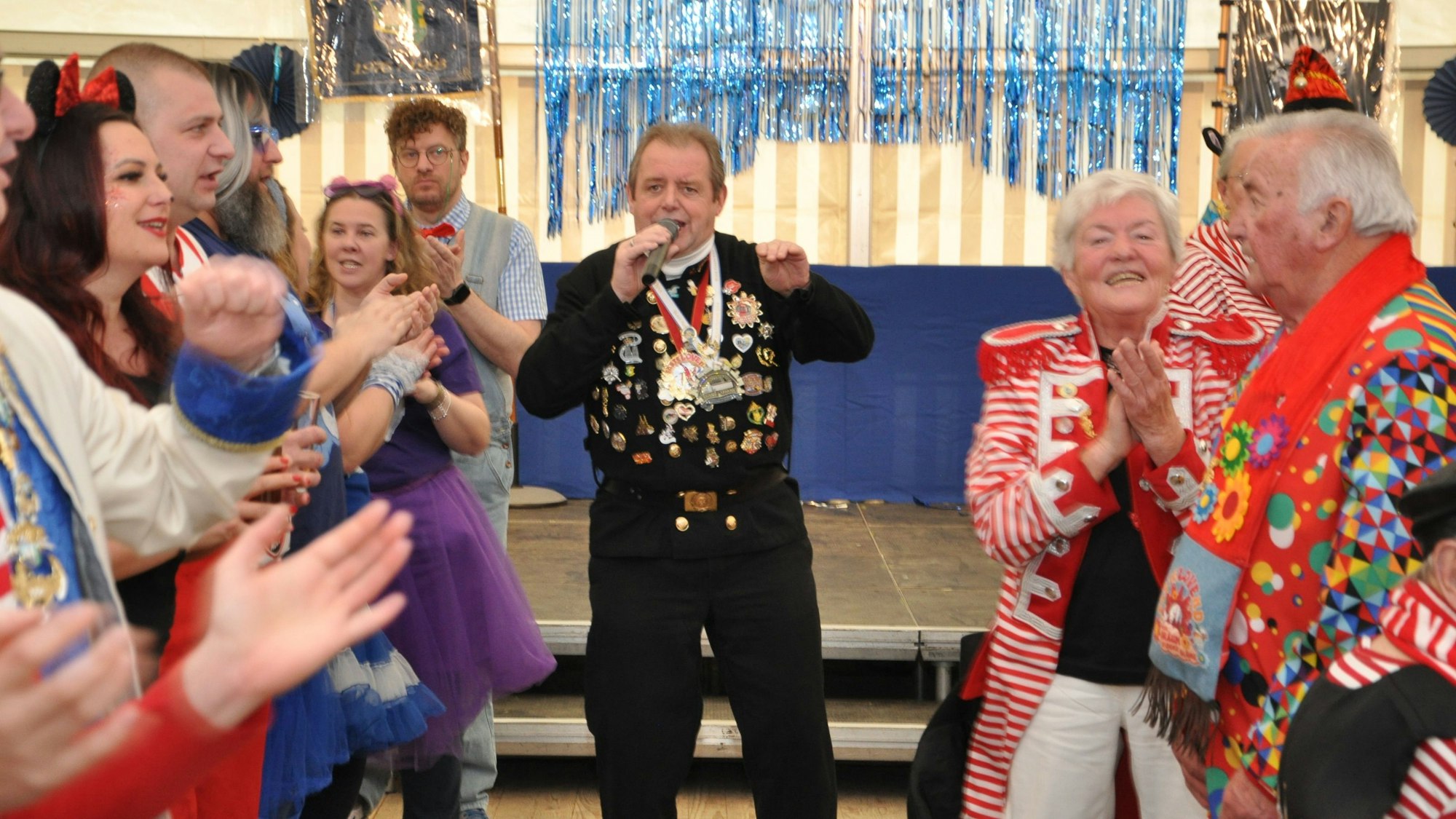 Um einen Mann mit Mikrofon stehen Menschen, die klatschen.