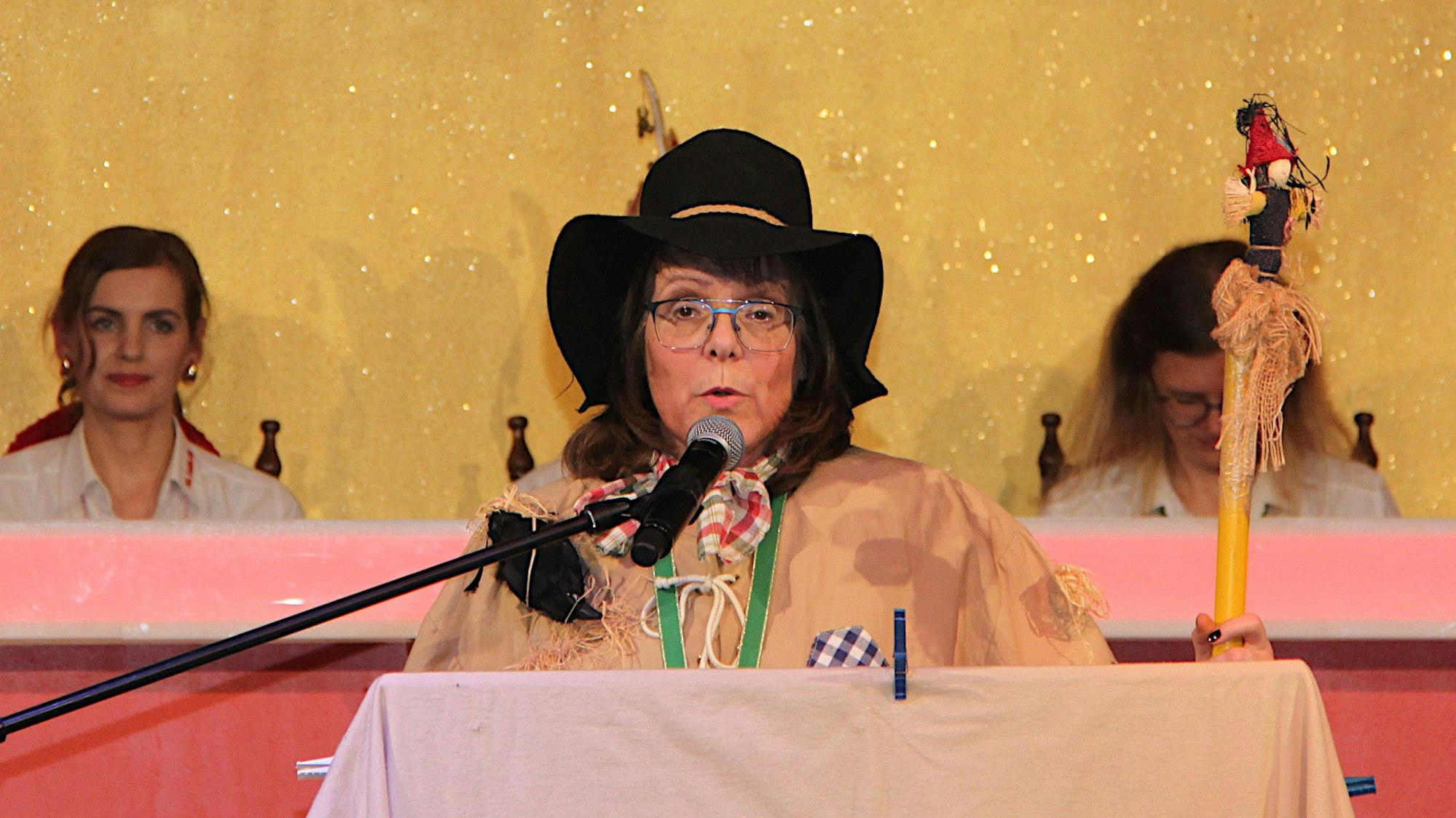Eine als Vogelscheuche verkleidete Frau steht am Rednerpult und spricht in ein Mikrofon.