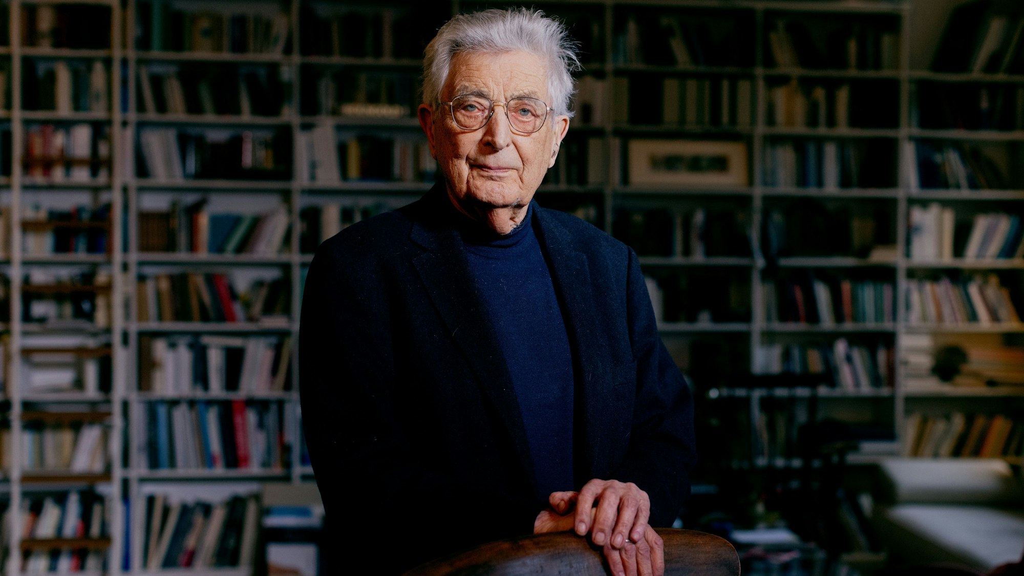 Gerhart Baum steht vor einer unscharf gestellten Bücherwand in seiner Wohnung in der Kölner Südstadt.