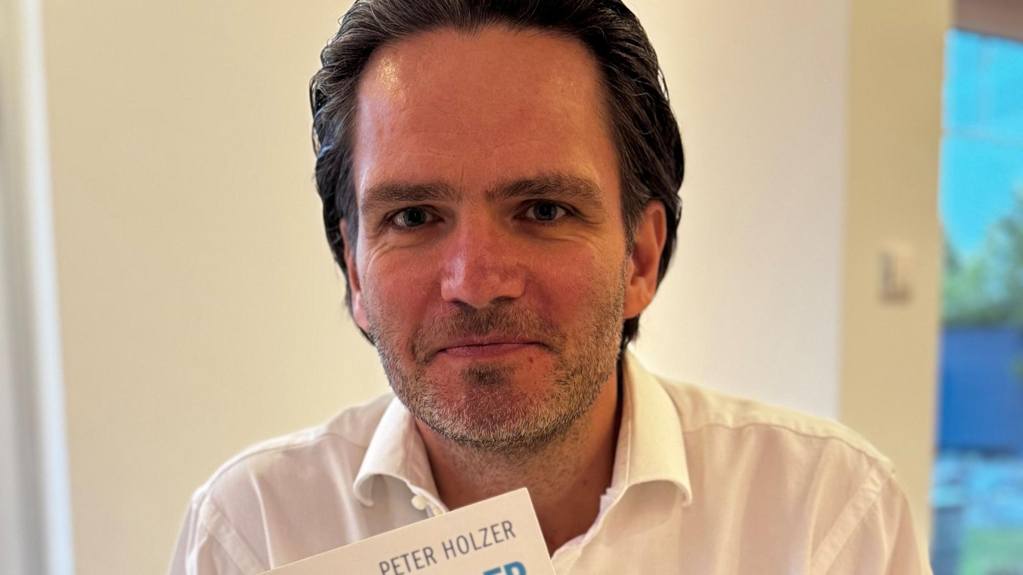 Auf dem Bild ist das Portrait eines Mannes mit einem Buch in der Hand zu sehen.