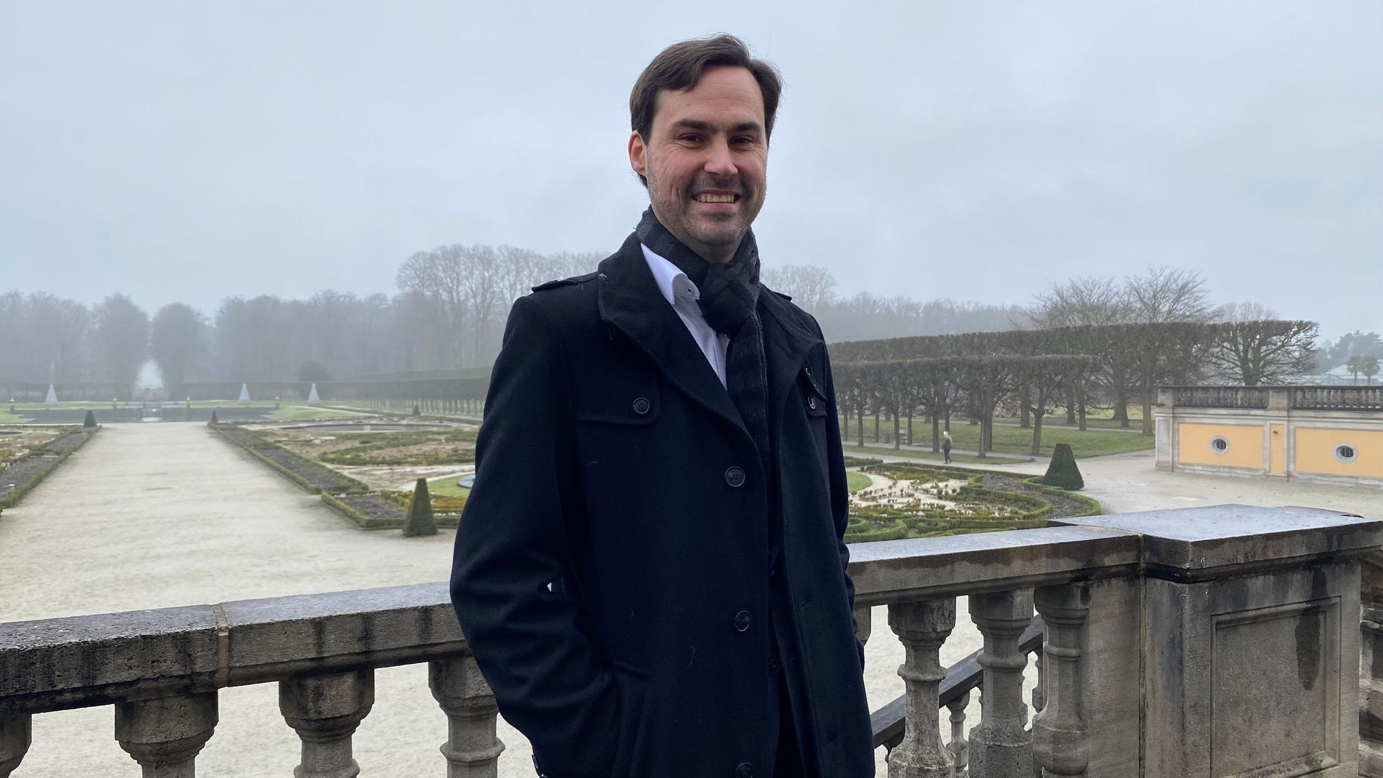 Markus Hausmann steht auf einer Terrasse, im Hintergrund ist der Schlosspark im Brühl zu sehen.