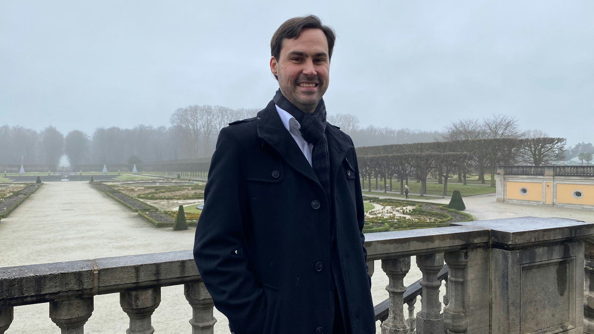Markus Hausmann steht auf einer Terrasse, im Hintergrund ist der Schlosspark im Brühl zu sehen.