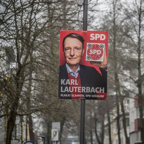Ein Wahlplakat von Karl Lauterbach an einem Mast Zwischen Häusern und Bäumen.