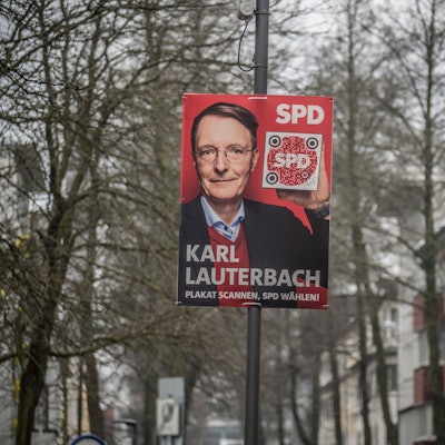 Ein Wahlplakat von Karl Lauterbach an einem Mast Zwischen Häusern und Bäumen.