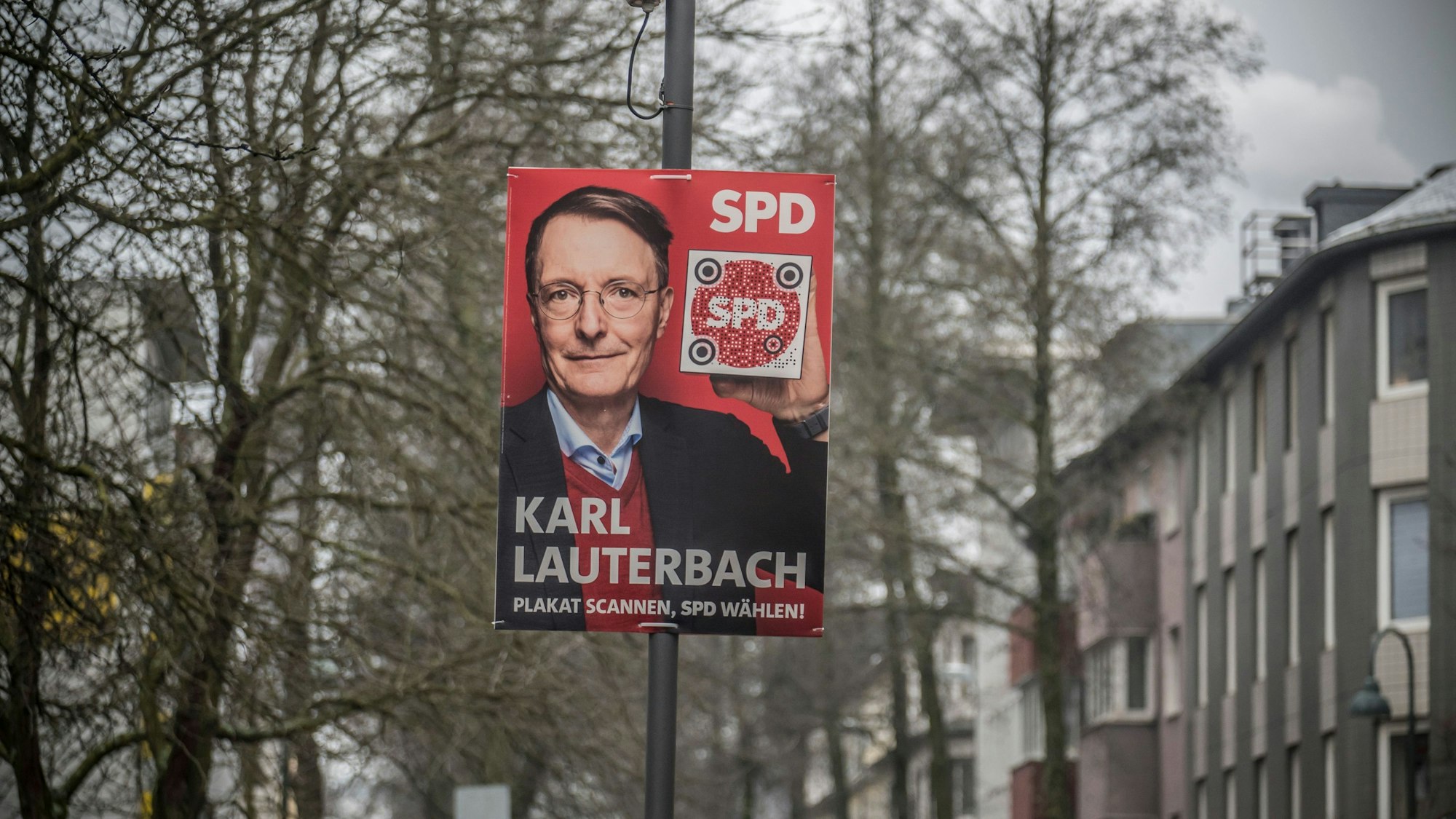 Ein Wahlplakat von Karl Lauterbach an einem Mast Zwischen Häusern und Bäumen.