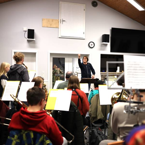 Orchesterleiterin Andrea Cosman steht im Musikheim am Dirigentenpult und dirigiert die jungen Musikerinnen und Musiker, die vor ihr sitzen.