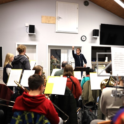 Orchesterleiterin Andrea Cosman steht im Musikheim am Dirigentenpult und dirigiert die jungen Musikerinnen und Musiker, die vor ihr sitzen.