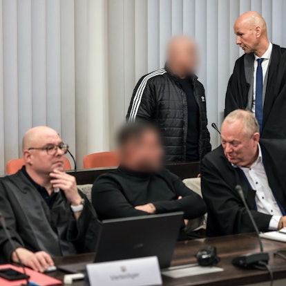 Der Hauptangeklagte (hinten, links) spricht im Gerichtssaal mit seinem Verteidiger Oliver Doelfs (hinten, rechts), während vorne ein Angeklagter (M) mit seinem Verteidiger Hartmut Moyzio (vorne, rechts) spricht.