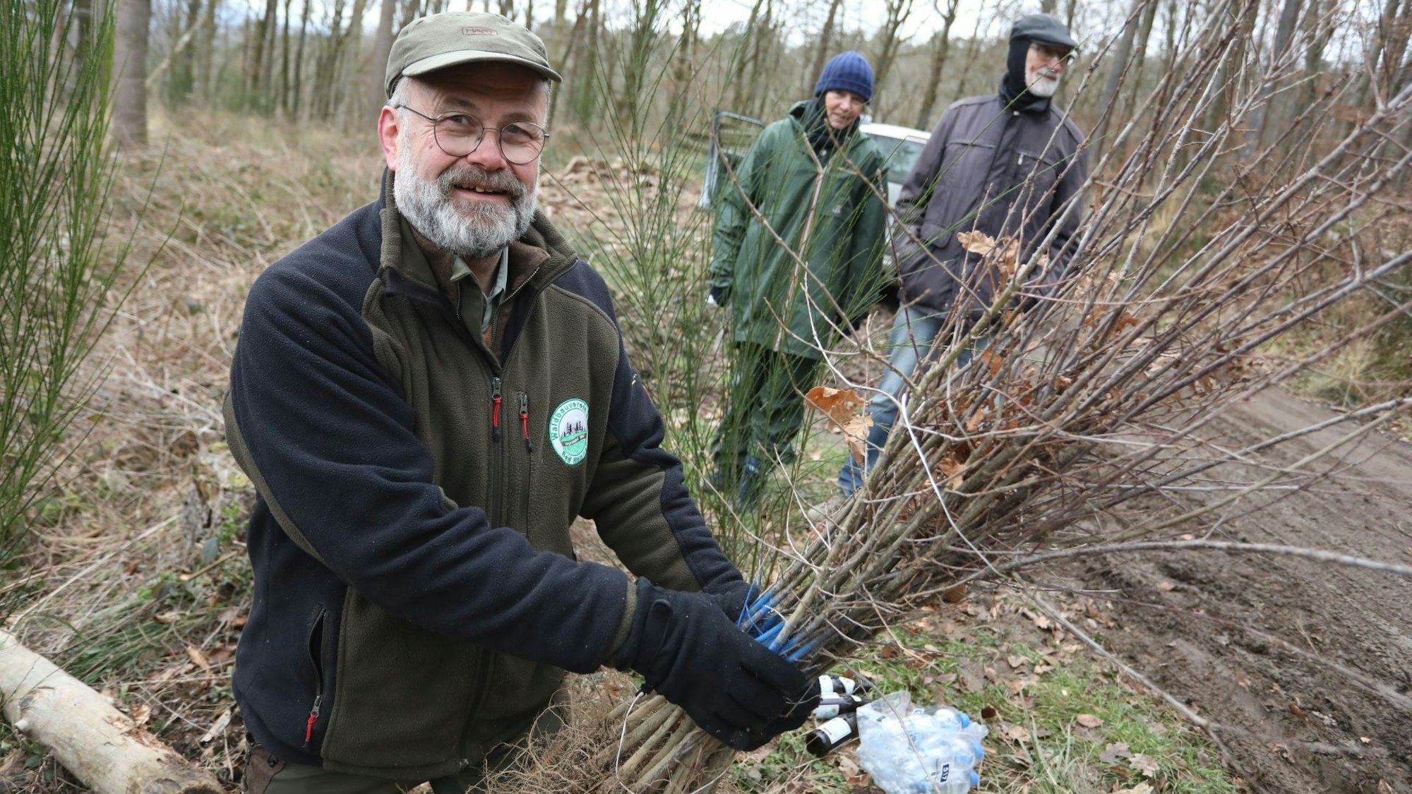 Ein Mann im Wald. In der Hand hält er Baumsetzlinge.