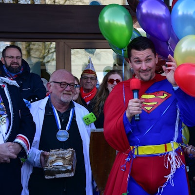 Ein Mann im Superman-Kostüm; an seiner Seite schweben Luftballons.