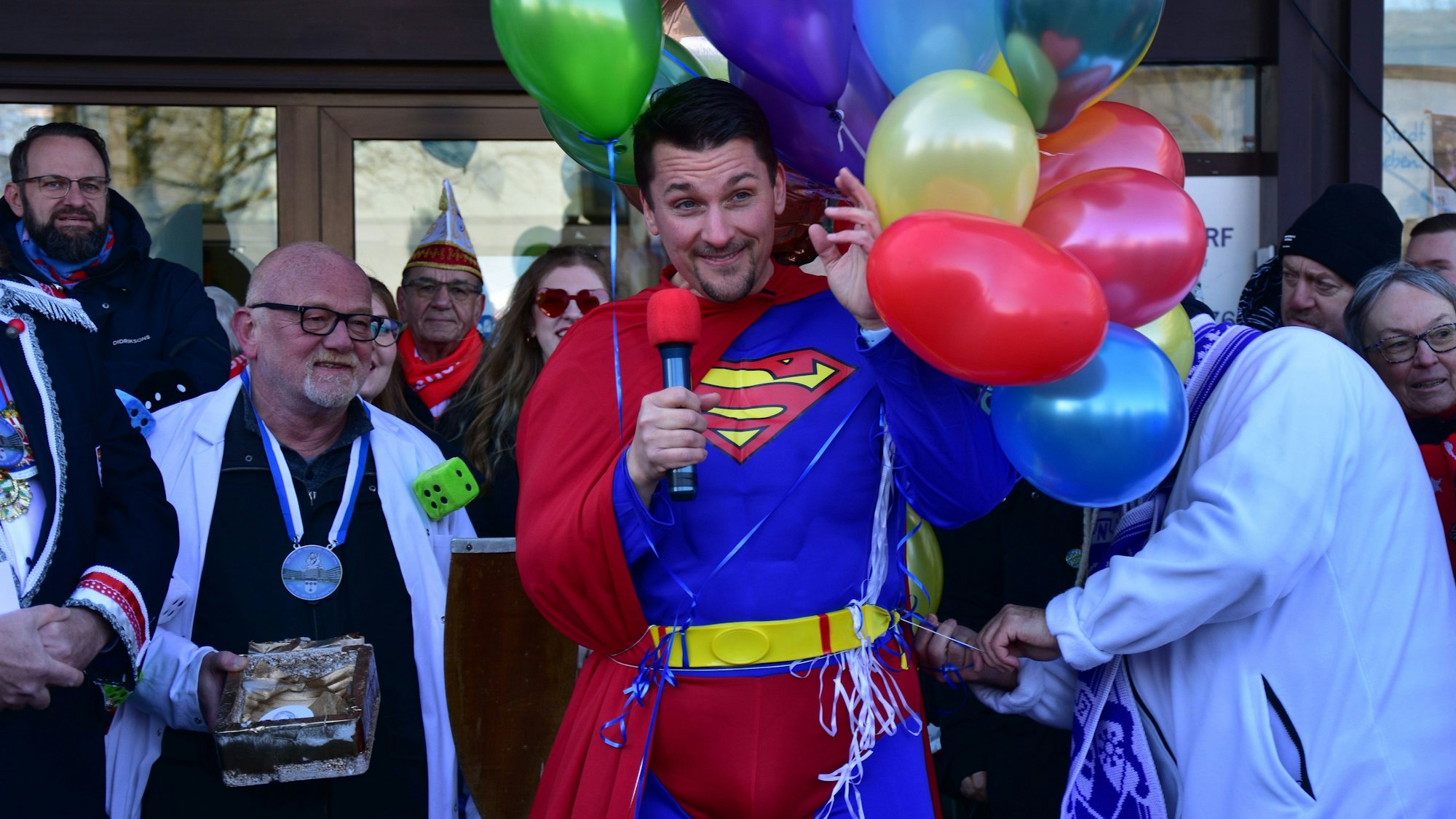 Ein Mann im Superman-Kostüm; an seiner Seite schweben Luftballons.