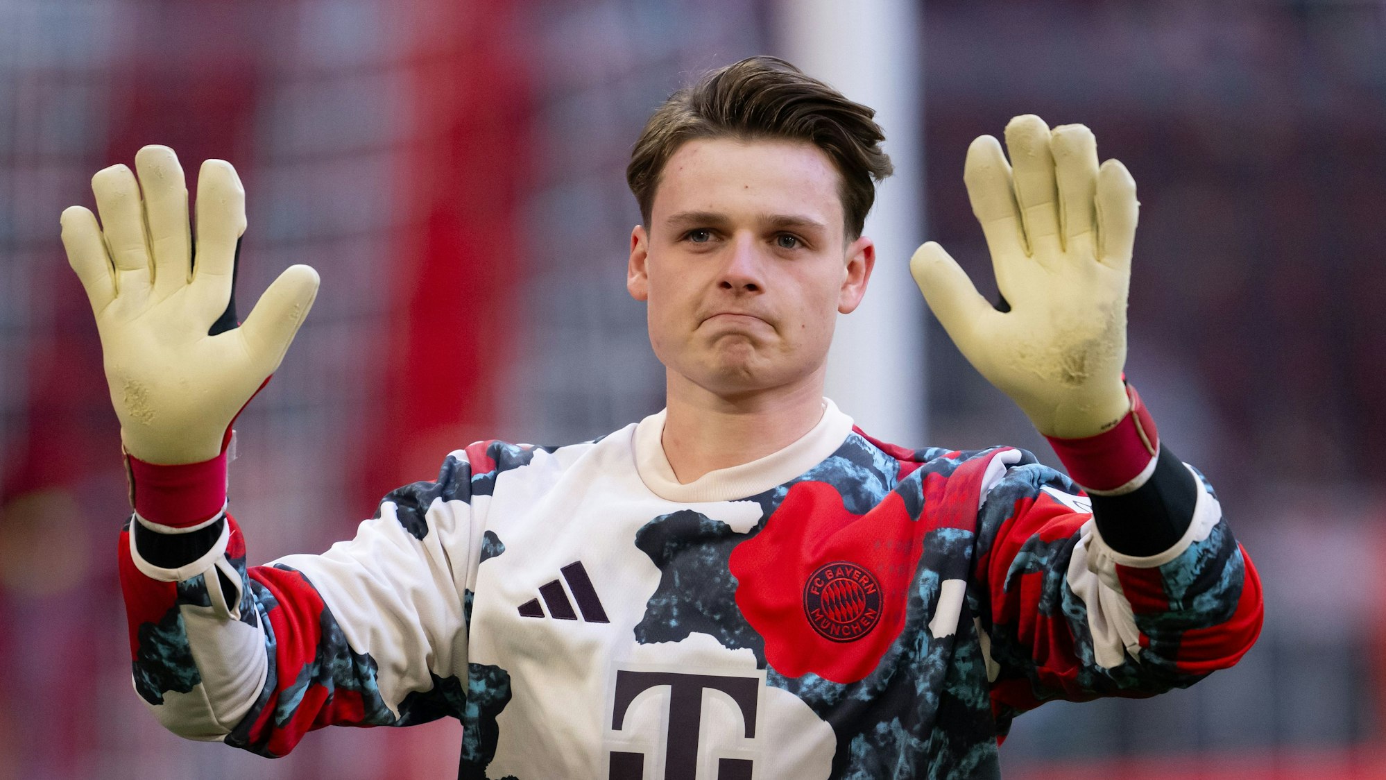 Torwart Jonas Urbig streckt beim Aufwärmtraining seine behandschuhten Hände nach vorn. Er trägt das Trikot des FC Bayern München.