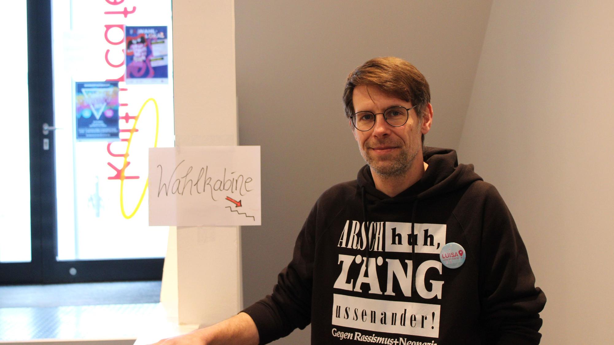 Ein Mann steht im Eingangsbereich des Siegburger Kulturcafés, im Hintergrund ist ein Schild mit der Aufschrift „Wahlkabine“ zu sehen.