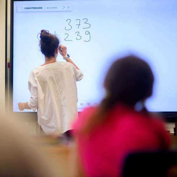 Eine Lehrerin schreibt eine Mathematikaufgabe auf eine digitale Schultafel.