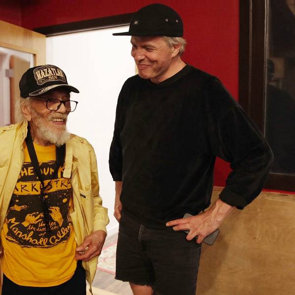 Jazz-Saxofonist Marshall Allen trägt ein gelbes offenes Hemd über einem dunkelgelben "Sun Ra Arkestra"-T-Shirt, rechts neben ihm steht Jan Lankisch, ganz in Schwarz, beide tragen Baseballkappen.