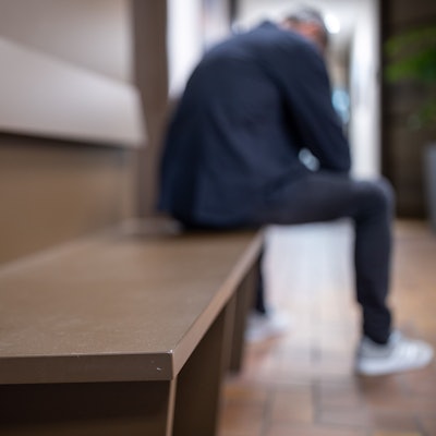 Ein Mann sitzt mit gesenktem Kopf auf einer Bank.