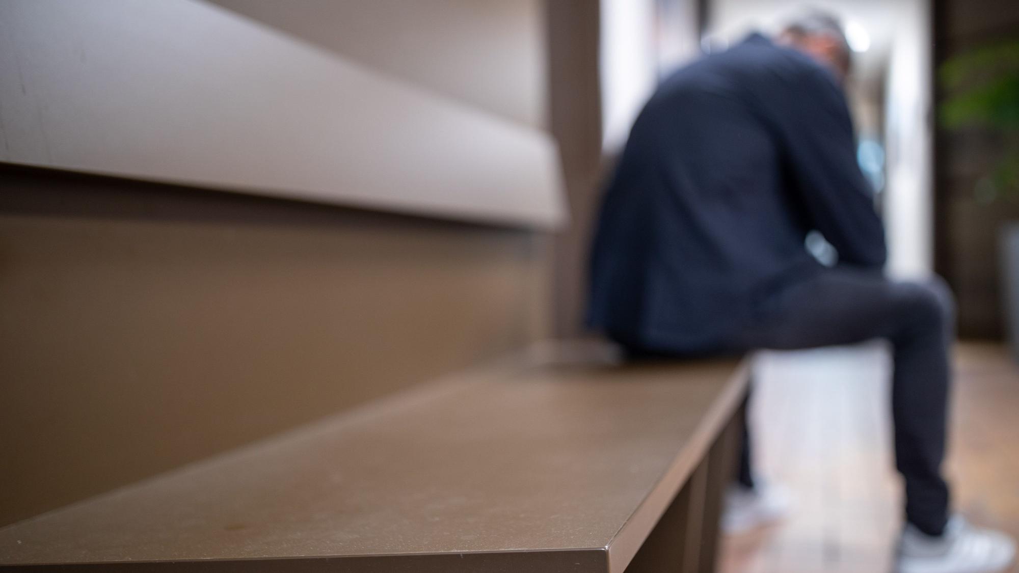Ein Mann sitzt mit gesenktem Kopf auf einer Bank.