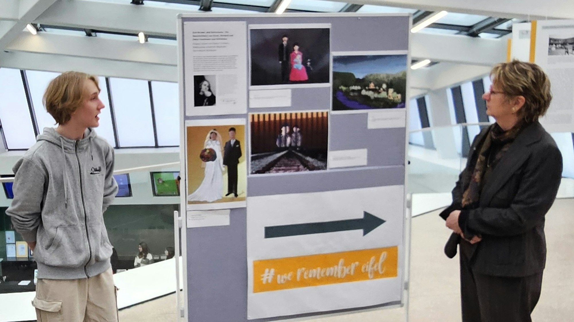 Hlynur Jakob Limbeck.und Silvia Löhrmann stehen vor einer fahrbaren Tafel mit seinen Bildern.