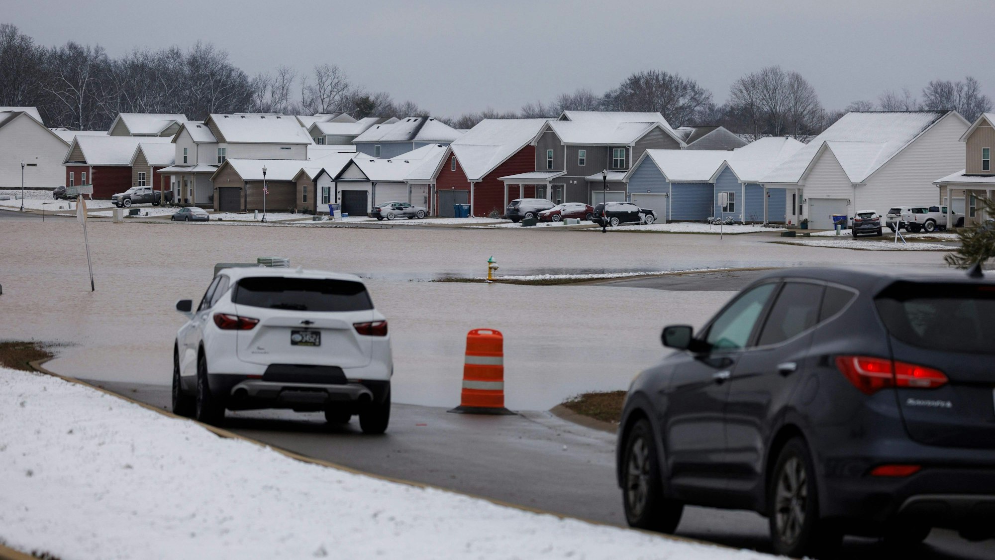 Autos stehen am Rand einer überfluteten Siedlung.