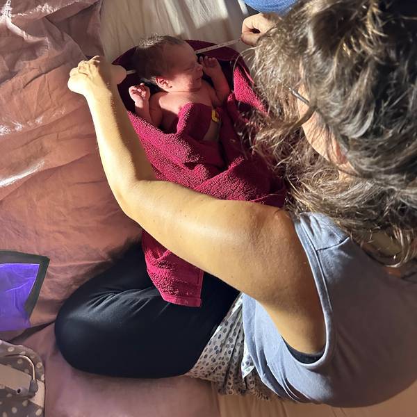 Ein Neugeborenes liegt in ein Handtuch gewickelt auf einem Bett und wird vermessen.