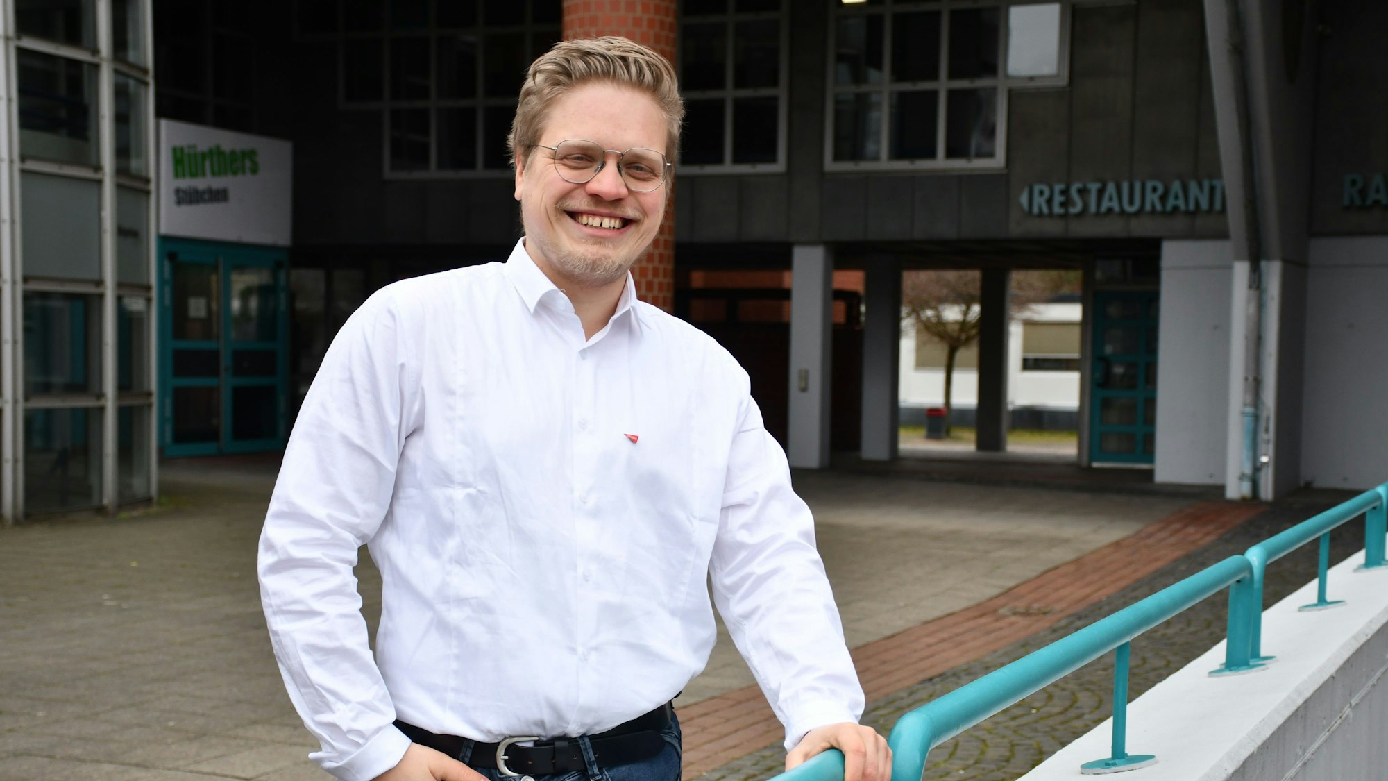 Das Foto zeigt den Kandidaten im weiße Hemd mit Linken-Button vor dem Bürgerhaus.