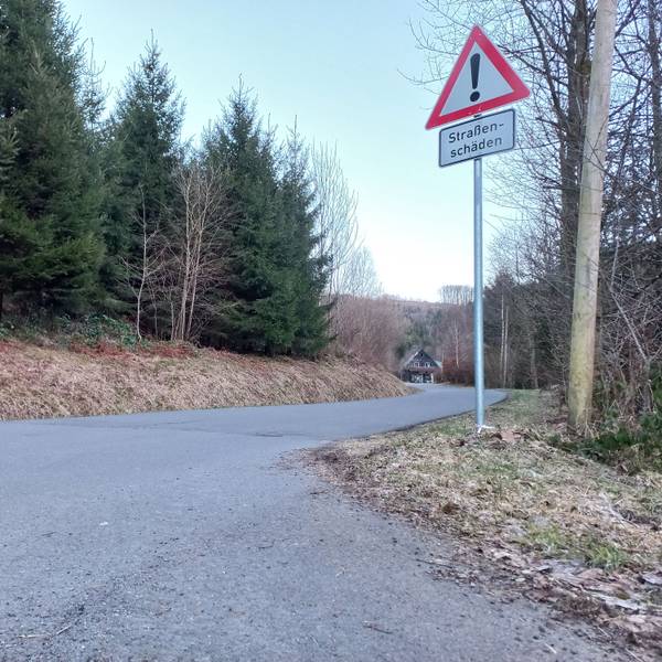 Blick auf eine Straße mit einem Schild, das vor Straßenschäden warnt.