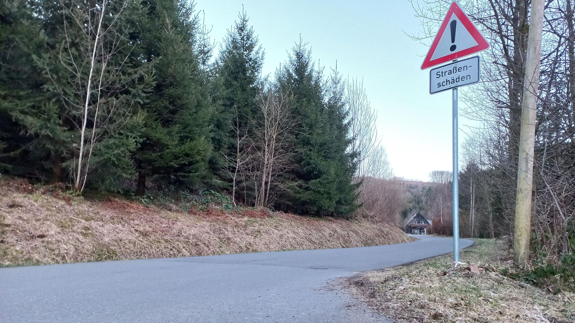 Blick auf eine Straße mit einem Schild, das vor Straßenschäden warnt.