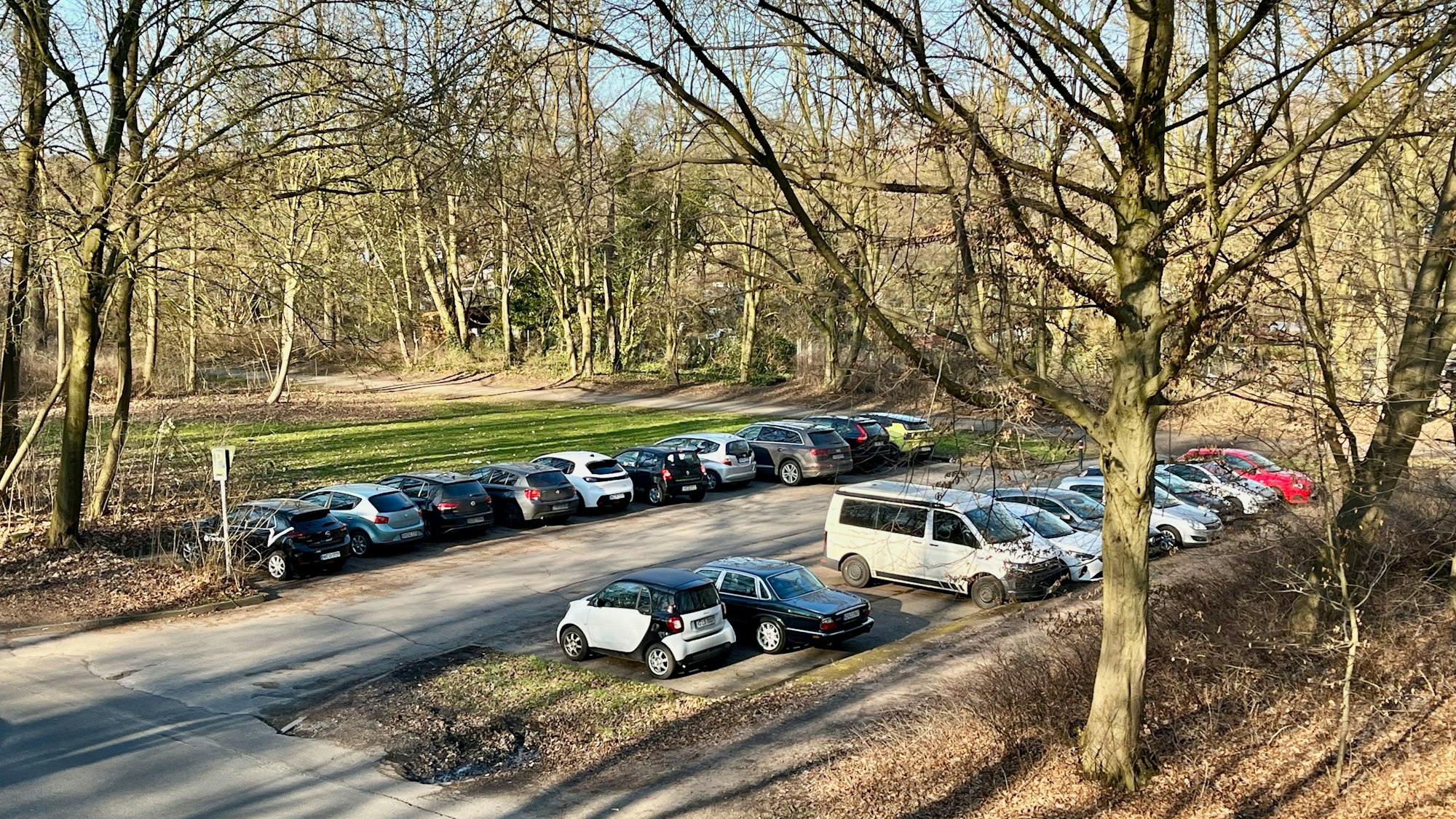 Blick auf einen Parkplatz, der an einen Wald und eine Grünanlage angrenzt