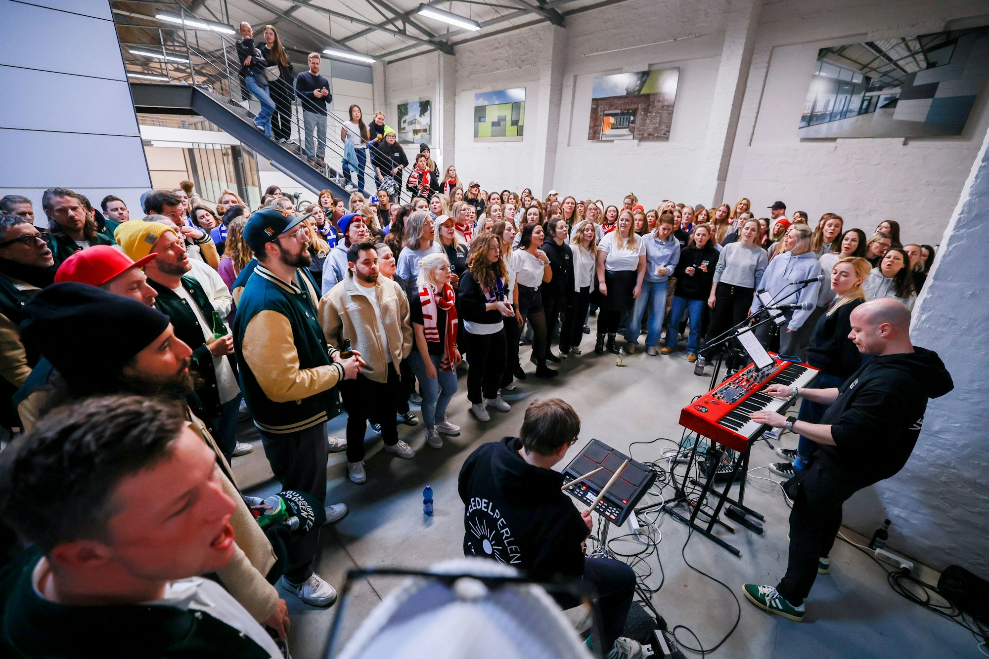 Männer und Frauen stehen in der Pattenhalle in einem Halbkreis um die beiden Chorleiter.