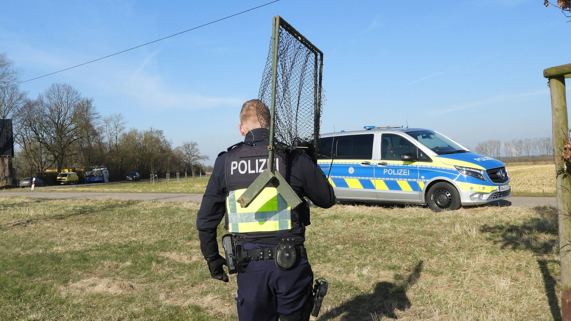 Das Foto zeigt einen Polizisten von hinten, der eine Vogelfalle trägt.