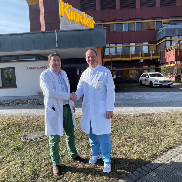 Zwei Ärzte schütteln sich vor einem Krankenhaus die Hände.